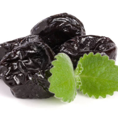 Heap of dried plums or prunes with a mint leaf isolated on white background.